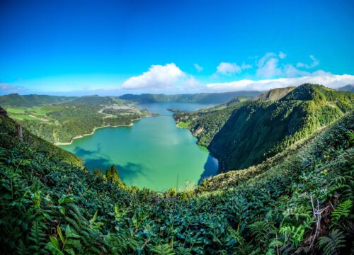 A mesmerizing view of the lake surrounded by mountains covered in green under the blue sky